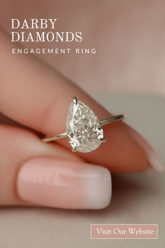 a woman's hand holding an engagement ring with a pear shaped diamond on it