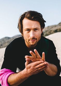 a man sitting on top of a sandy beach next to a pink object in his hand