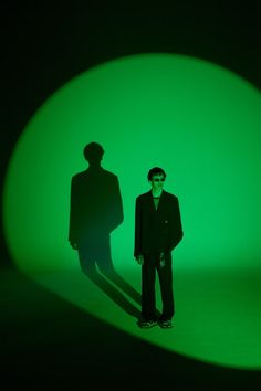 a man standing in front of a green light with his shadow on the wall behind him