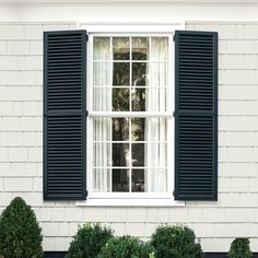 an open window with blue shutters on the side of a white brick building and potted plant in front