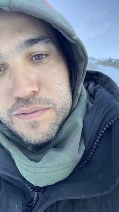 a man wearing a hooded jacket and looking at the camera with a snowy landscape in the background