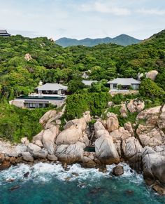 an aerial view of a house on top of a hill next to the ocean with waves crashing in front of it