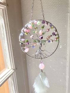 a wind chime with beads and feathers hanging from it's side in front of a window