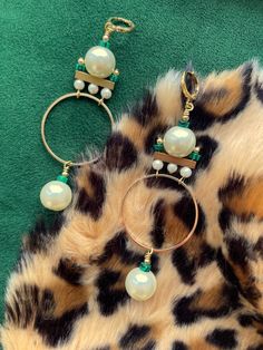 These gorgeous and unique statement hoops were designed in the art deco style of the 1920's. These are the perfect earrings for dressing up your holiday attire.These hoop earrings hang approximately 3.5" from the lobe and measure approximately 1.25" inches at their widest point. The design contains 12mm faux pearls, 4mm faux pearls, 3mm malachite heishi beads, and gold plated brass components.The leverback closure is 22k gold plated and should be suitable for sensitive ears. These are semi-light