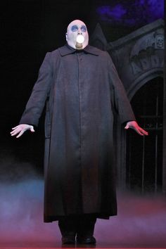 a man in a long coat and mask standing on stage with his hands out to the side