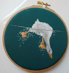 a white bird with orange beaks flying through the air on a green background in an embroidered hoop