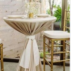 the table is set up with gold chairs and white linen draped over it, as well as vases filled with flowers