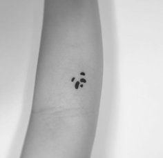 a black and white photo of a person's arm with a small paw tattoo on it