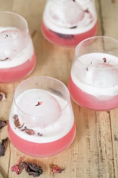 three glasses filled with pink liquid sitting on top of a wooden table next to dried flowers