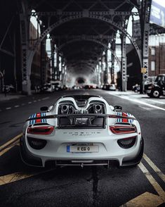 a white sports car parked on the side of a road under an overpass with cars behind it