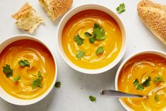 three bowls of soup with bread and parsley garnish on the side next to them