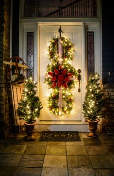 a christmas wreath on the front door of a house decorated with lights and evergreens