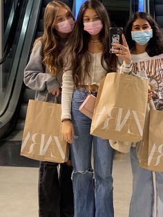 three girls wearing face masks and holding shopping bags in front of an escalator