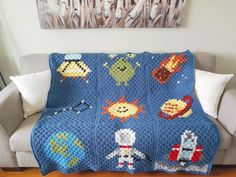 a blue crocheted blanket with small cartoon characters on it sitting on a couch