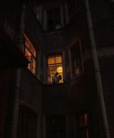 two people are standing in the window of an old building at night with their lights on