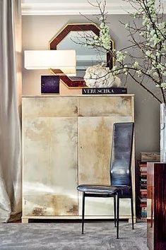 a living room with a chair, vase and flowers on the sideboard in front of a mirror