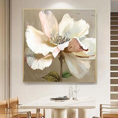 a large white flower sitting on top of a table in front of a wall mounted painting