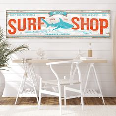 a surf shop sign hanging on the wall above a table with two chairs and a potted plant