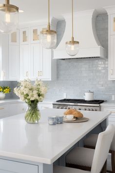 a kitchen with white cabinets and marble counter tops, gold pendant lights over the island