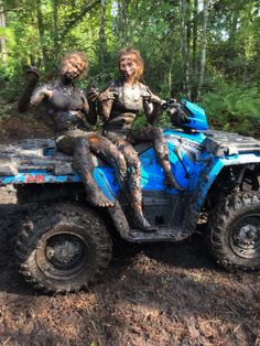 two people riding on the back of a blue four - wheeler in mud covered forest