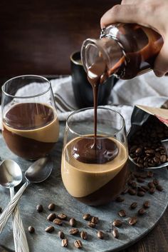 someone pouring chocolate into two glasses on top of a plate with coffee beans and spoons