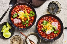 two bowls of chili with sour cream, limes and tortillas on the side