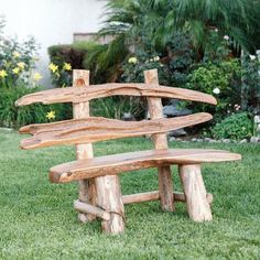 a wooden bench made out of logs sitting in the grass next to some flowers and trees