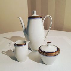 three white teapots sitting on top of a table next to each other with gold trim