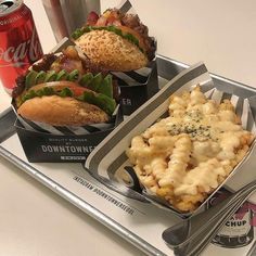 two trays filled with different types of food on top of a metal tray next to cans of soda