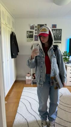 a woman taking a selfie in the mirror while wearing a denim jacket and hat