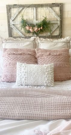 a bed with pink and white pillows on top of it next to a wooden headboard