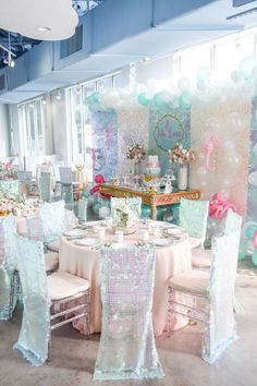 a room filled with lots of tables covered in white and pink decorations next to balloons