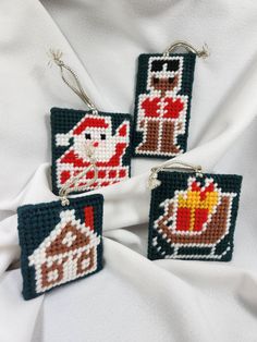 three cross stitch ornament ornaments hanging on a white fabric background, each decorated with an image of santa claus and his house