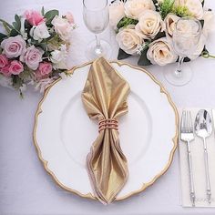 the table is set with white and gold plates, silverware, and pink flowers