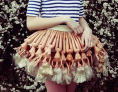 a woman is wearing a skirt made out of fake human legs and bones, with flowers in the background