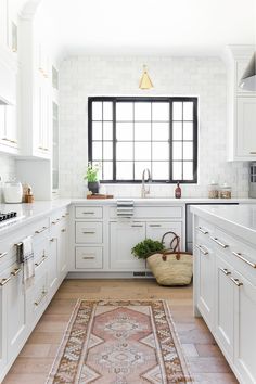 a kitchen with white cabinets and an area rug on the floor in front of the window