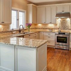 a large kitchen with white cabinets and granite counter tops on the island in front of the sink