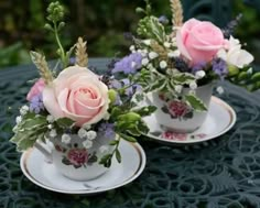 two white cups with pink roses and greenery on them sitting on a table outside