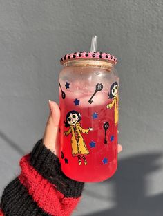 a person holding up a red mason jar with drawings on it