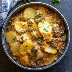 a bowl filled with stew and potatoes on top of a black table next to a blue towel