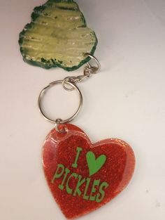 i pickles heart shaped keychain sitting on top of a white table next to a piece of broccoli