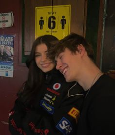 a man and woman are smiling together in front of a wall with signs on it