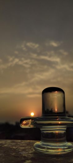 the sun is setting in the distance behind a glass container with a lid on it