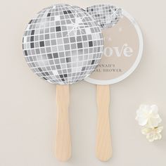 two wooden paddles and a mirror ball on a white surface with flowers next to it