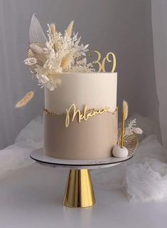 a white cake with gold lettering and flowers on top is sitting on a silver platter