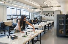 a woman is working on some art work in a large room with lots of windows