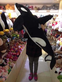 a woman holding an orca whale stuffed animal in front of a store filled with stuffed animals