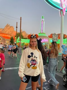 a woman standing in the middle of an amusement park at night with mickey mouse ears on her head