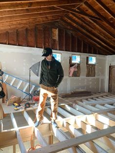 a man standing on top of a wooden floor in a room with unfinished walls and beams