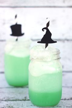 two mason jars filled with green liquid and topped with black witches hat topper sticks